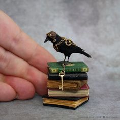 a tiny black bird sitting on top of a stack of books with a gold key