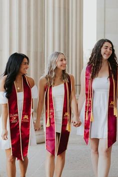 three women in graduation gowns holding hands and walking down the street with one another