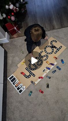 a young boy sitting on the floor next to a cardboard sign that says boss with cars around it