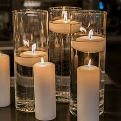 several lit candles sitting on top of a table next to glass vases filled with water