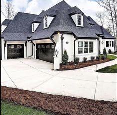 a large white house with black garage doors and two story windows on the front of it