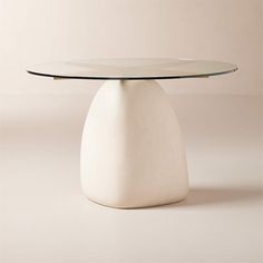 a white table with a glass top and gold trimmings on the base, against a beige background