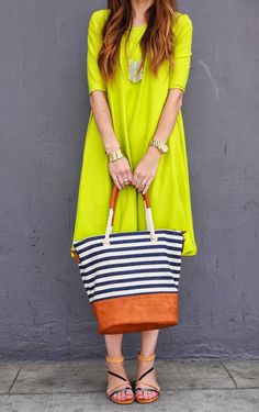 a woman is holding a striped bag in front of a gray wall and wearing sandals