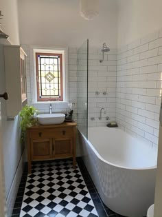 a white bath tub sitting next to a sink under a window in a tiled bathroom