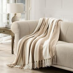 a couch with a blanket on top of it next to a coffee table and lamp