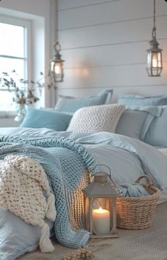 a bed with blue blankets and pillows next to a lit candle in a wicker basket