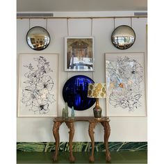 there are three pictures hanging on the wall above two tables with lamps and vases