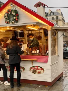 two women are standing in front of a small food stand with lights on the roof