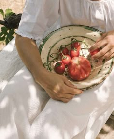 a woman holding a plate with tomatoes on it in her hands while sitting down outside