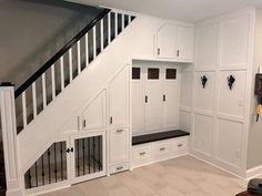 a room with white cabinets and drawers under the stairs