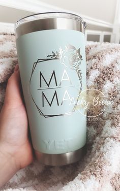 a person holding a cup with the word mam on it in front of a blanket