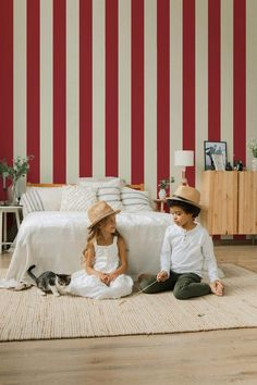 two children are sitting on the floor in front of a red and white striped wall