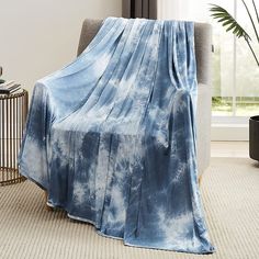 a blue and white blanket sitting on top of a chair next to a plant in a living room