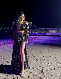 a woman standing on top of a sandy beach next to a purple lit building at night