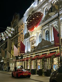 a red sports car parked in front of a large building with christmas lights on it