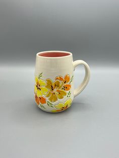 a coffee cup with yellow flowers painted on the outside and red inside, sitting on a gray surface