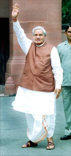 an old man in a brown and white outfit waves to the camera while standing next to another man