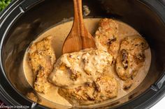 chicken with gravy in a slow cooker being stirred by a wooden spoon