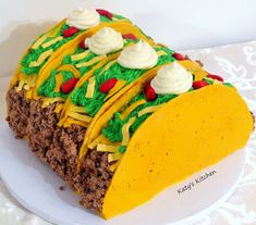 a taco cake on a white plate with yellow icing and green frosting