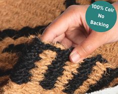 a hand is holding onto a black and tan crocheted rug with the words 100 % off on it