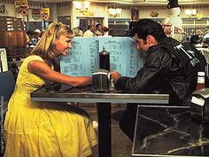 a man and woman sitting at a table in front of a soda machine talking to each other