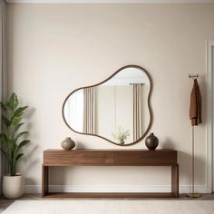 a mirror on the wall above a wooden table with a vase and potted plant