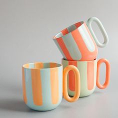 three colorful cups sitting next to each other on top of a gray surface with one cup in the middle