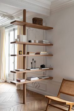 a wooden shelf with books on top of it in front of a white wall and window