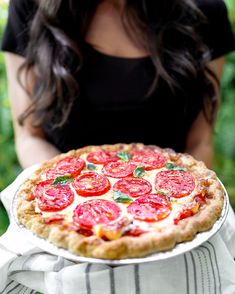 a woman holding a pizza with tomatoes on it