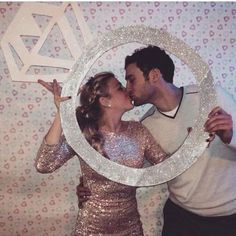 a man and woman are kissing in front of a photo frame with the letter s on it