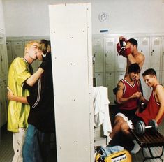 three men in lockers with one holding a bottle and the other looking at his cell phone