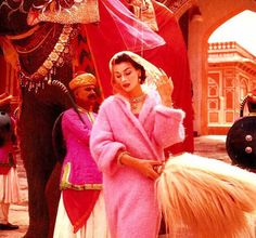 a woman in a pink dress standing next to a man with a horse on the street