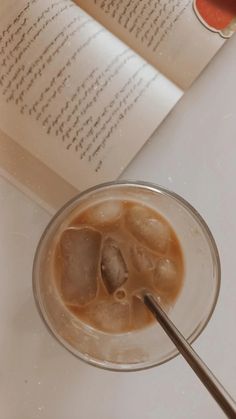 an open book sitting on top of a table next to a glass filled with liquid