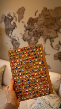 a person holding up a brown book with lots of different buttons on it in front of a world map