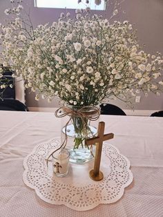 a vase filled with white flowers and a wooden cross on top of a doily