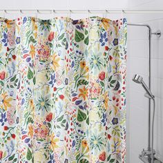 a shower curtain with colorful flowers and leaves on it in a white tiled bath room