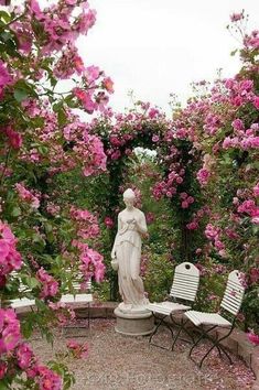 a statue in the middle of a garden with pink flowers around it and lawn chairs