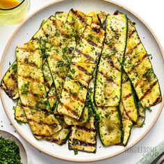 grilled zucchini with parsley on a plate next to a glass of orange juice