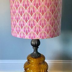 a lamp with a pink shade on it sitting on top of a wooden table next to a blue wall