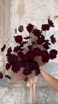 a hand holding a bouquet of flowers in front of a stone wall