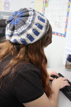 a woman sitting at a desk typing on a keyboard and wearing a knitted hat