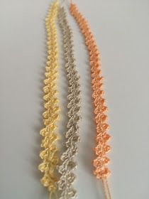 three different colored crocheted necklaces on a white surface with an orange, yellow, and silver chain