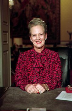 an older woman sitting at a desk smiling