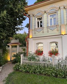 a white house with red flowers in the window boxes and a picket fence around it