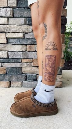 a person with tattoos on their legs and feet standing next to a brick wall wearing brown shoes