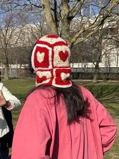 a woman wearing a red and white crocheted hat standing next to a tree