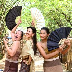 three women in traditional thai garb are holding up umbrellas and posing for the camera