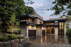 a modern house with stone walls and large windows on the front, surrounded by trees