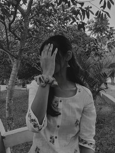 black and white photograph of woman covering her face with both hands while standing in front of tree