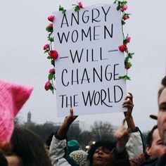 a group of people holding up signs with flowers on them and one person wearing a pink hat